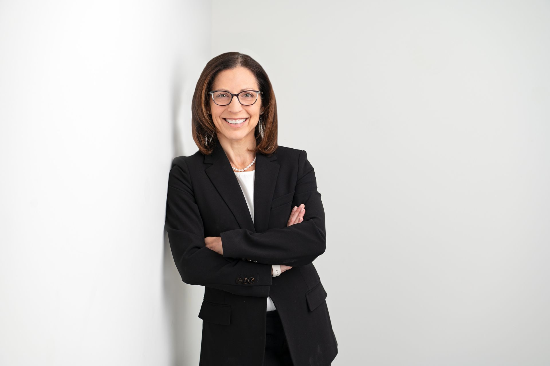 Four women in athletic wear, smiling and embracing in a room with a window and a large plant.