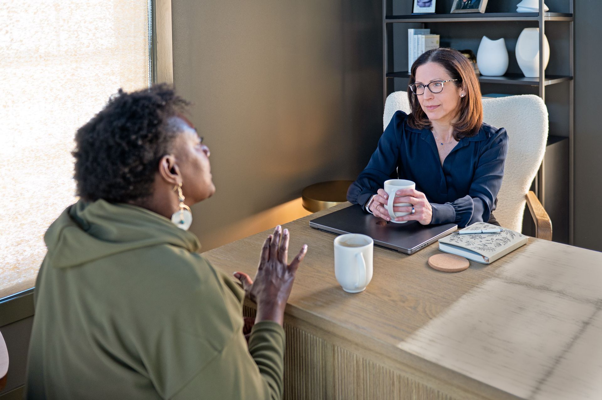 Three women pose together. Two wear blazers; one embraces the others. All wear lanyards. Indoors, conference setting.