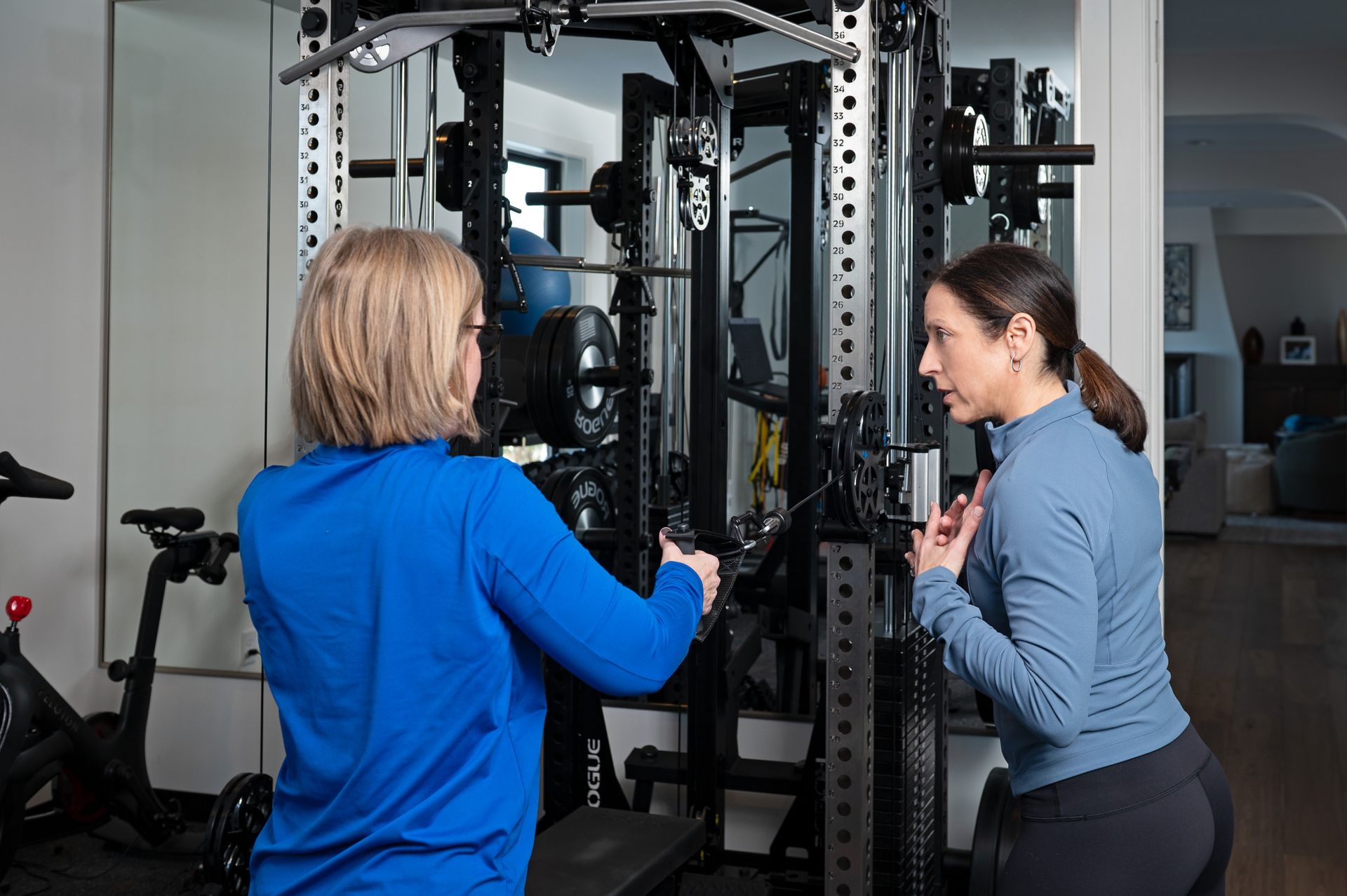 Woman using a cable machine; trainer observing in home gym.