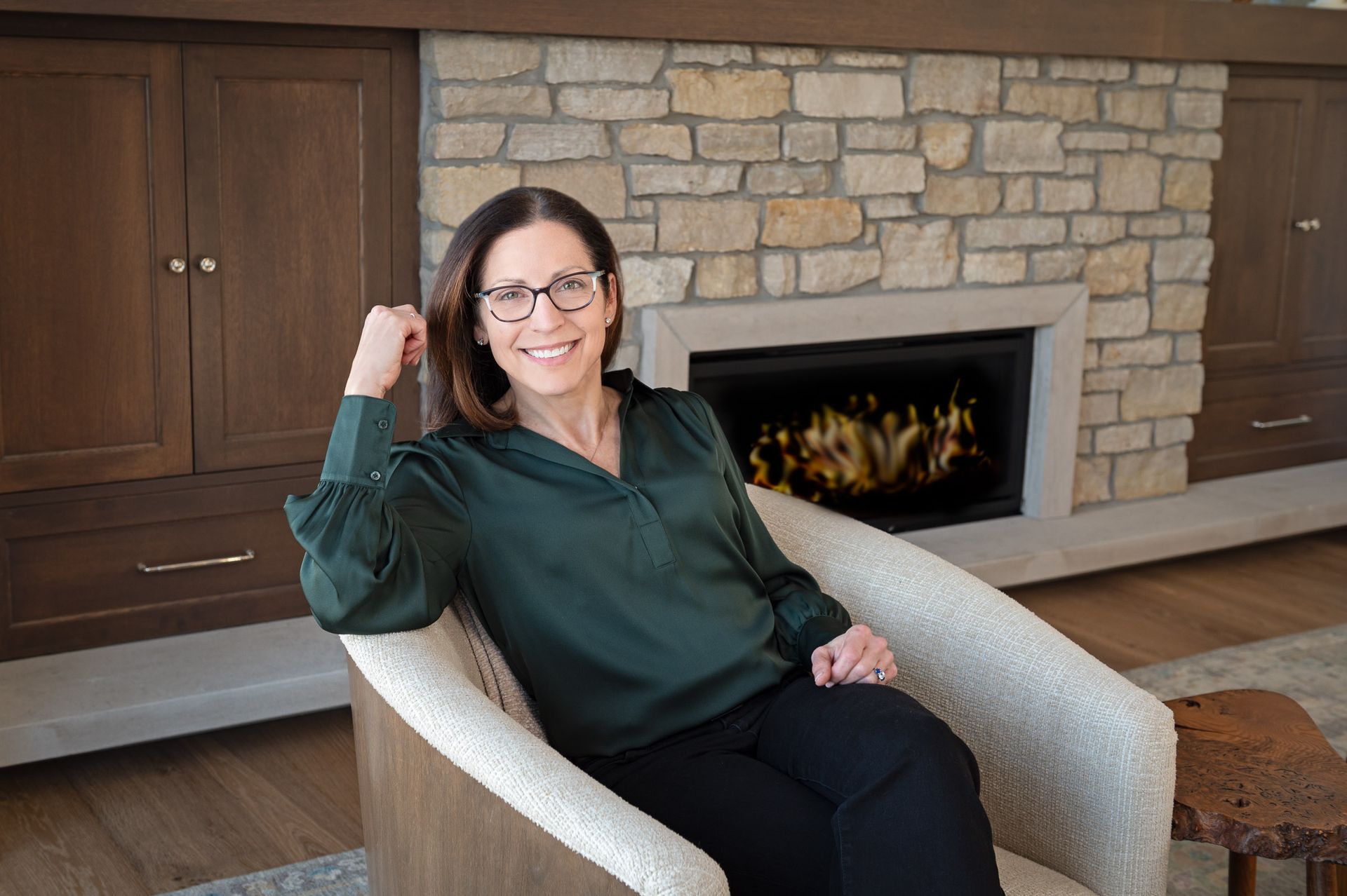Four women in athletic wear, smiling and embracing in a room with a window and a large plant.