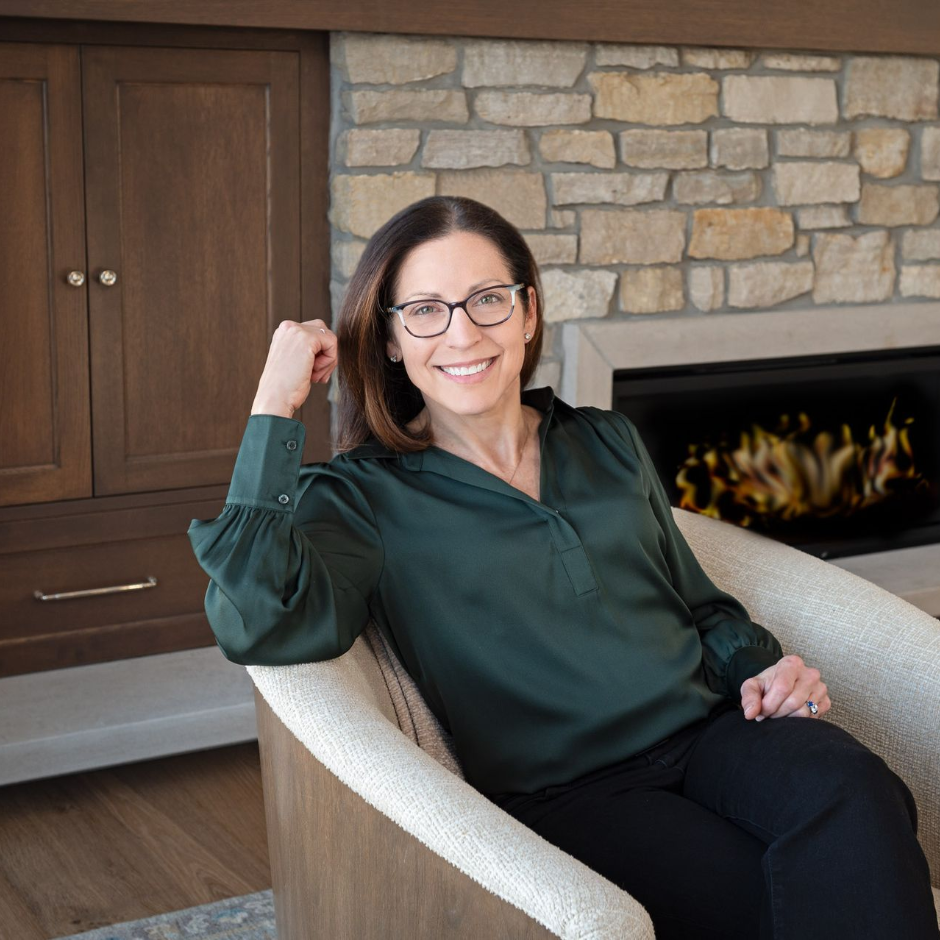 Woman holding mug, smiles warmly. Standing in kitchen with neutral tones and natural light.