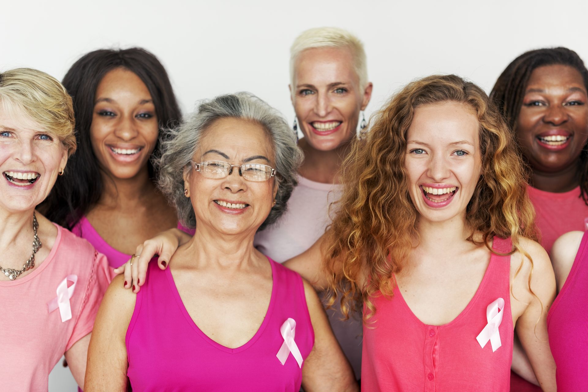Woman holding a pink ribbon, eyes closed, smiling, against a gray background.