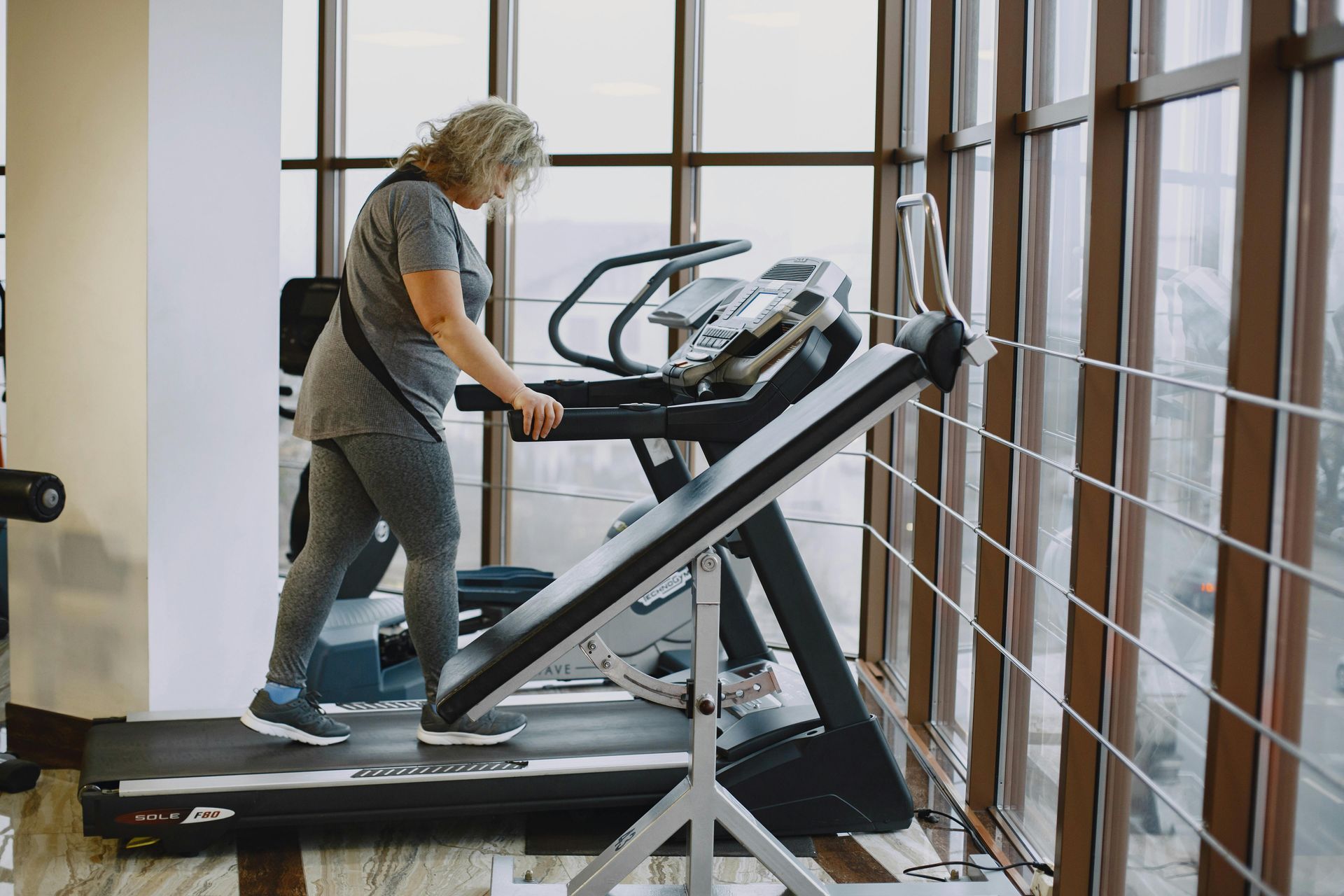 Woman in workout clothes on a treadmill in a gym, holding onto the handrail.