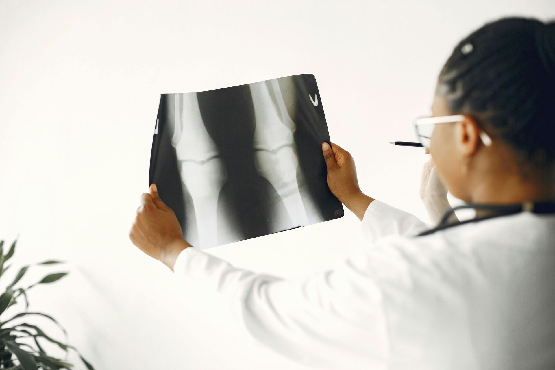 Doctor examining an X-ray of a knee, wearing a white coat and glasses.