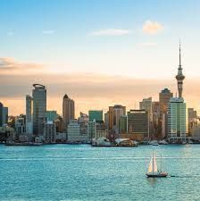 Horizonte de Auckland, Nova Zelândia, com a Sky Tower ao pôr do sol e veleiro na água.