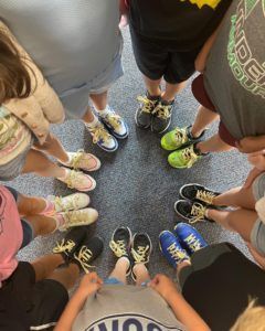 A group of children are standing in a circle with their shoes on the floor