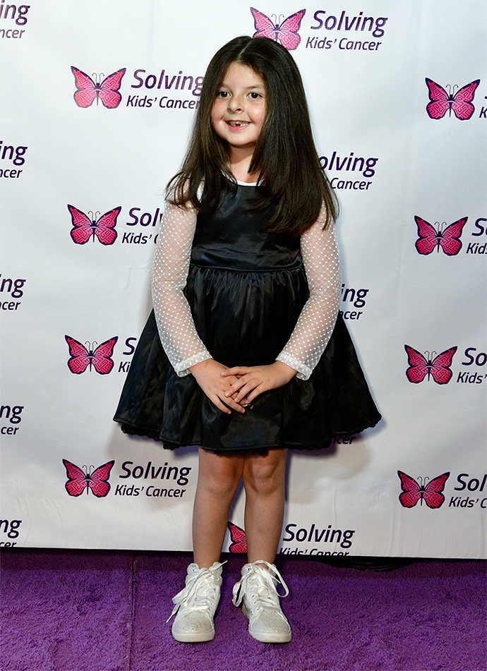 A little girl in a black dress is standing on a purple carpet.
