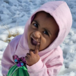 A baby in a pink hoodie is holding a watermelon in the snow