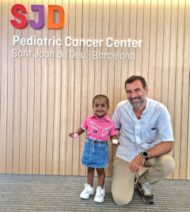 A man and a little girl pose in front of a sign that says sjd pediatric cancer center
