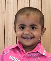 A little boy wearing a pink shirt is smiling for the camera.