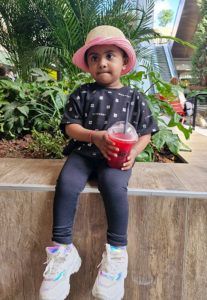 A little girl is sitting on a ledge holding a drink.