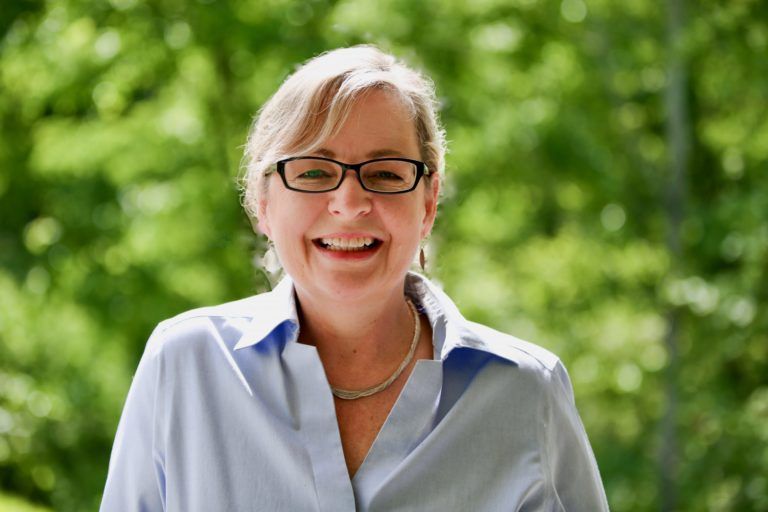 A woman wearing glasses and a blue shirt is smiling for the camera.
