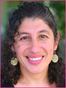 A woman with curly hair is smiling and wearing earrings