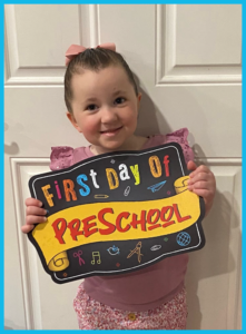 A little girl is holding a sign that says first day of preschool