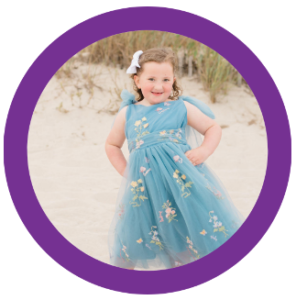 A little girl in a blue dress is standing on a sandy beach.