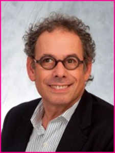A man wearing glasses and a suit smiles for the camera