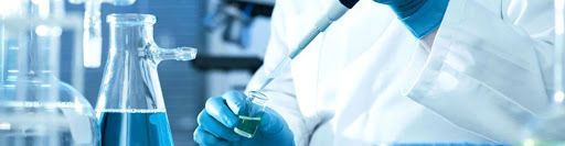 A scientist is holding a pipette and a beaker in a laboratory.