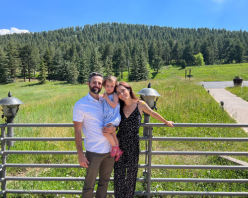 A family posing for a picture in front of a fence with trees in the background.