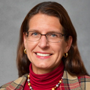 A woman wearing glasses and a red turtleneck smiles for the camera