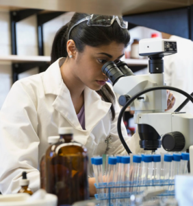 A woman in a lab coat looks through a microscope