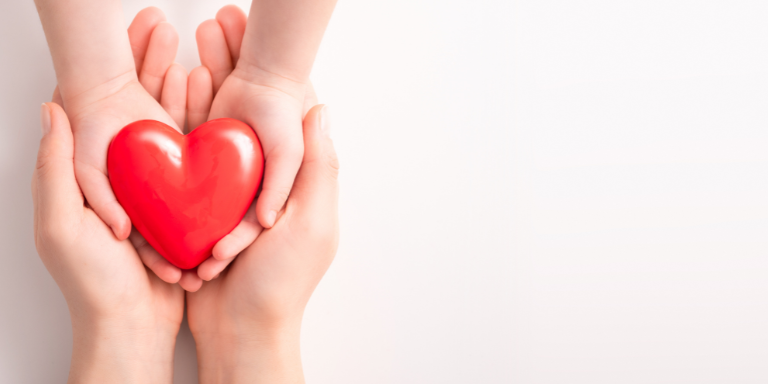 A woman and child are holding a red heart in their hands.