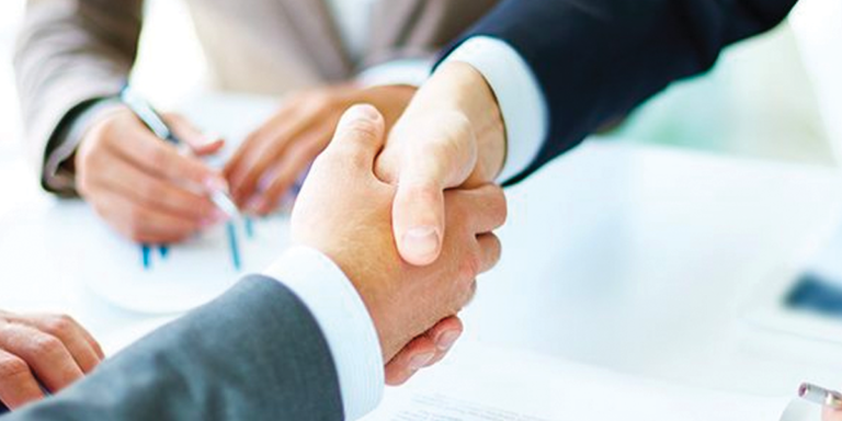 A group of business people are shaking hands over a table.