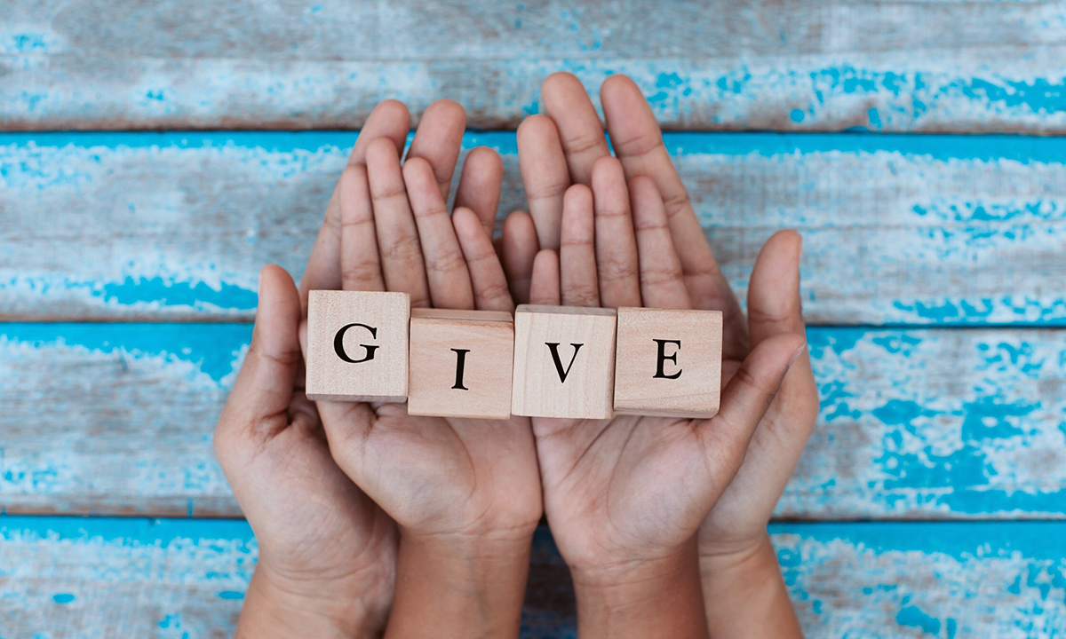 A couple of hands holding wooden blocks that spell out the word give.