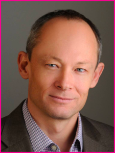 A man in a suit and plaid shirt smiles for the camera
