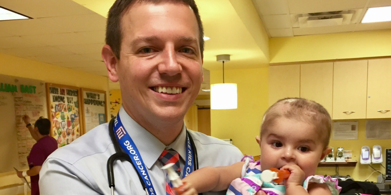 A doctor is holding a baby in his arms and smiling.