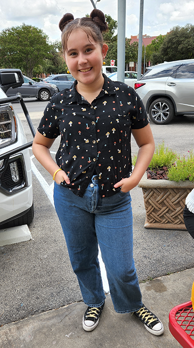 A young girl is standing in a parking lot with her hands in her pockets.