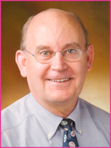 A bald man wearing glasses and a tie smiles for the camera