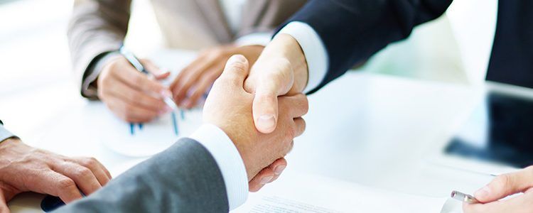 A group of business people are shaking hands over a table.