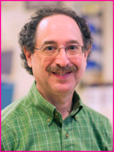 A man wearing glasses and a green plaid shirt smiles for the camera