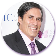 A man in a suit and tie is smiling in front of an ic logo