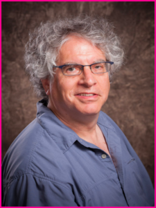 A man with curly hair and glasses is wearing a blue shirt
