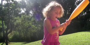 A little girl in a pink dress is holding a baseball bat