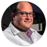 A bald man wearing glasses and a white lab coat is in a circle.