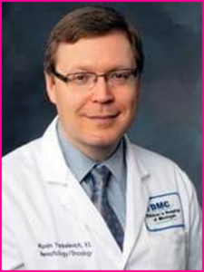 A man in a white lab coat and tie is smiling for the camera