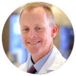 A man in a white coat and tie is smiling in a circle.