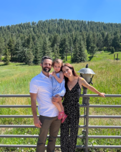 A family posing for a picture in front of a fence with trees in the background.