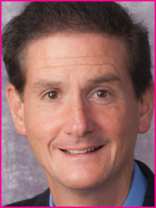 A man in a suit and blue shirt smiles for the camera