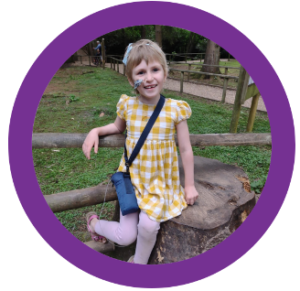 A little girl in a yellow dress is sitting on a tree stump