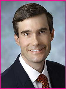 A man wearing glasses and a suit looks at the camera
