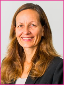 A woman with long brown hair is smiling and wearing a black jacket