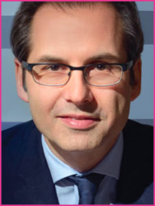 A man wearing glasses and a suit looks at the camera