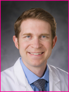 A man in a white coat and tie smiles for the camera