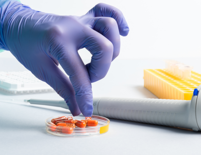 A person wearing purple gloves is putting pills in a petri dish.