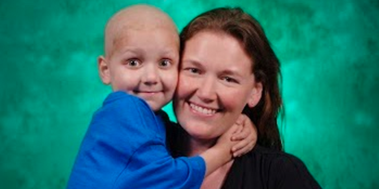 A woman is holding a child with cancer in her arms.