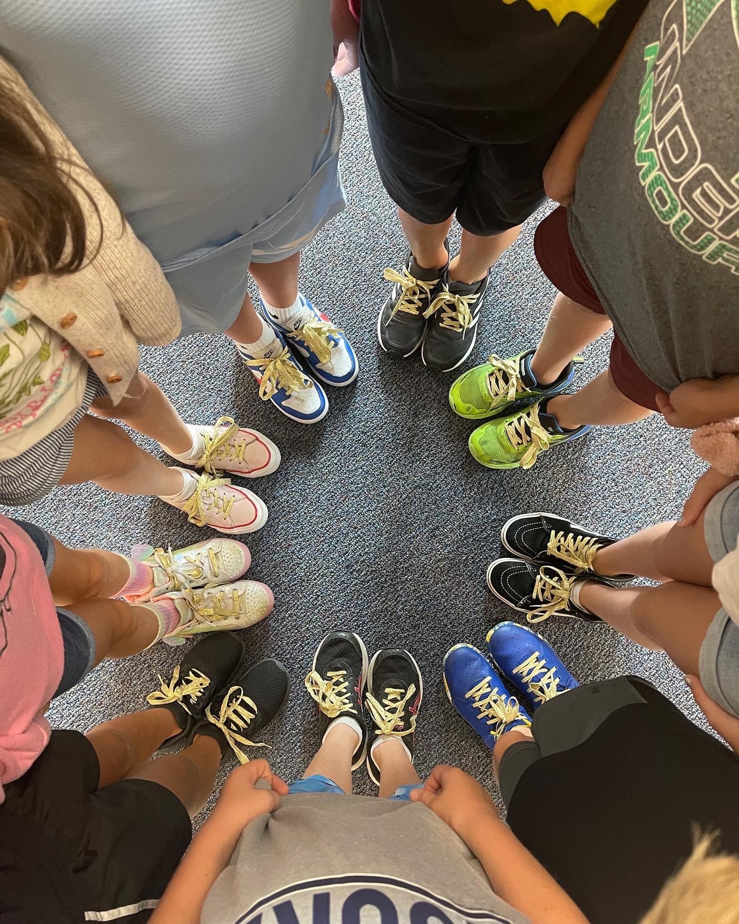 A group of children are standing in a circle with their shoes on the floor.