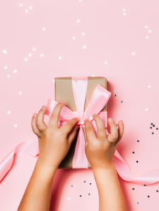 A child is holding a gift box with a pink bow.